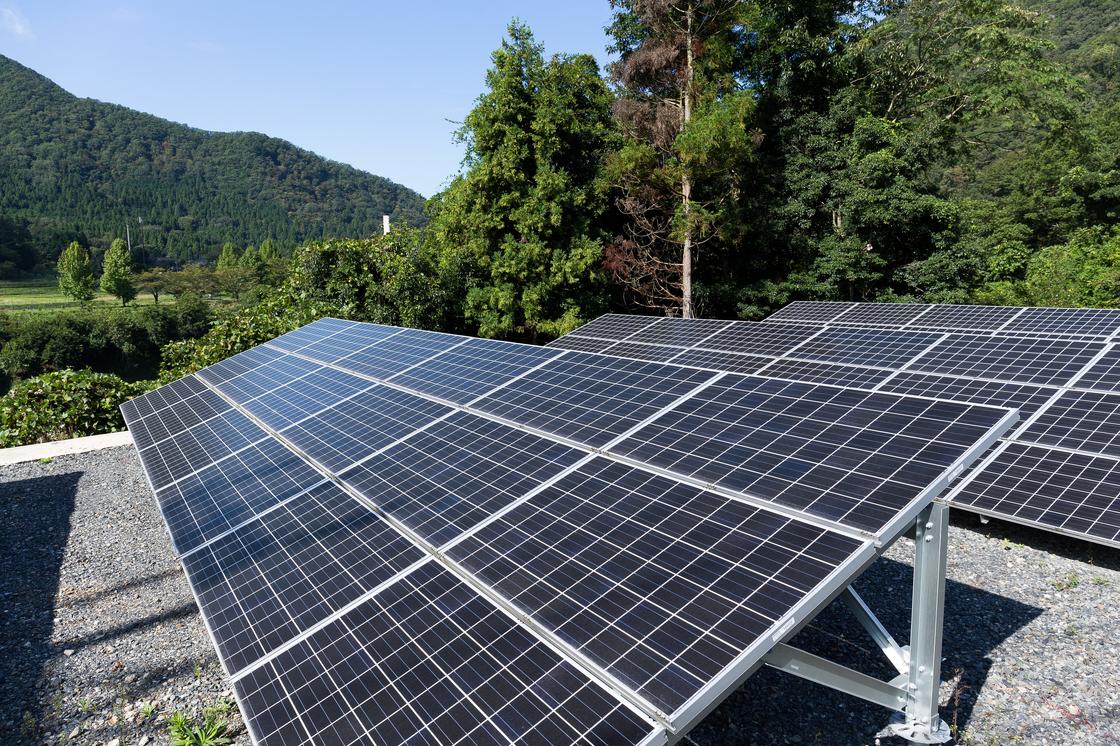 An array of solar panels mounted on a rooftop surrounded by lush green trees and mountains.